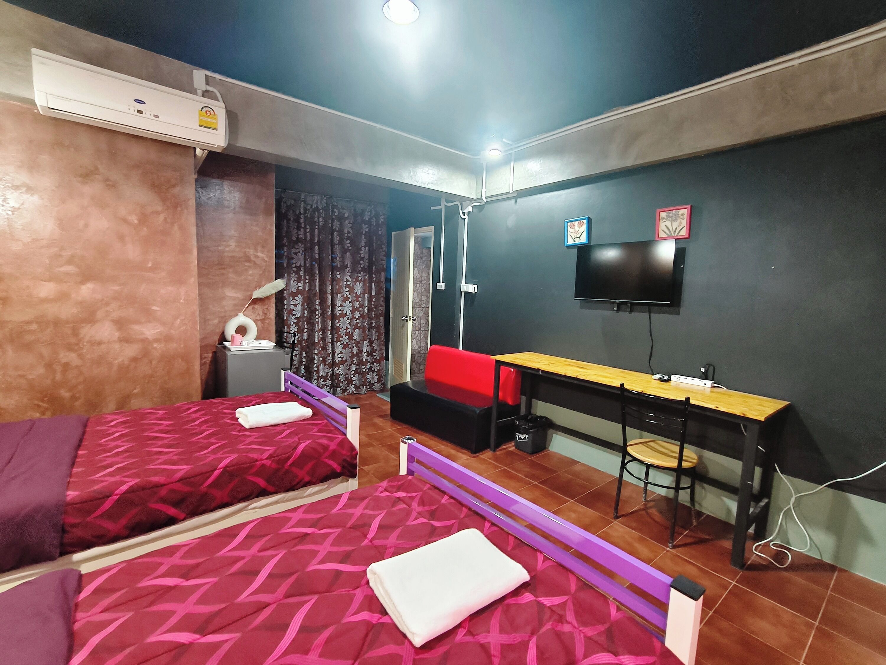 A room with two beds, a desk, a chair, a TV, and an air conditioner.