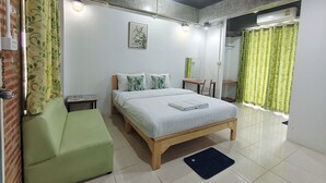 Un dormitorio con cama, una silla verde, un escritorio de madera, un espejo y la puerta del baño.