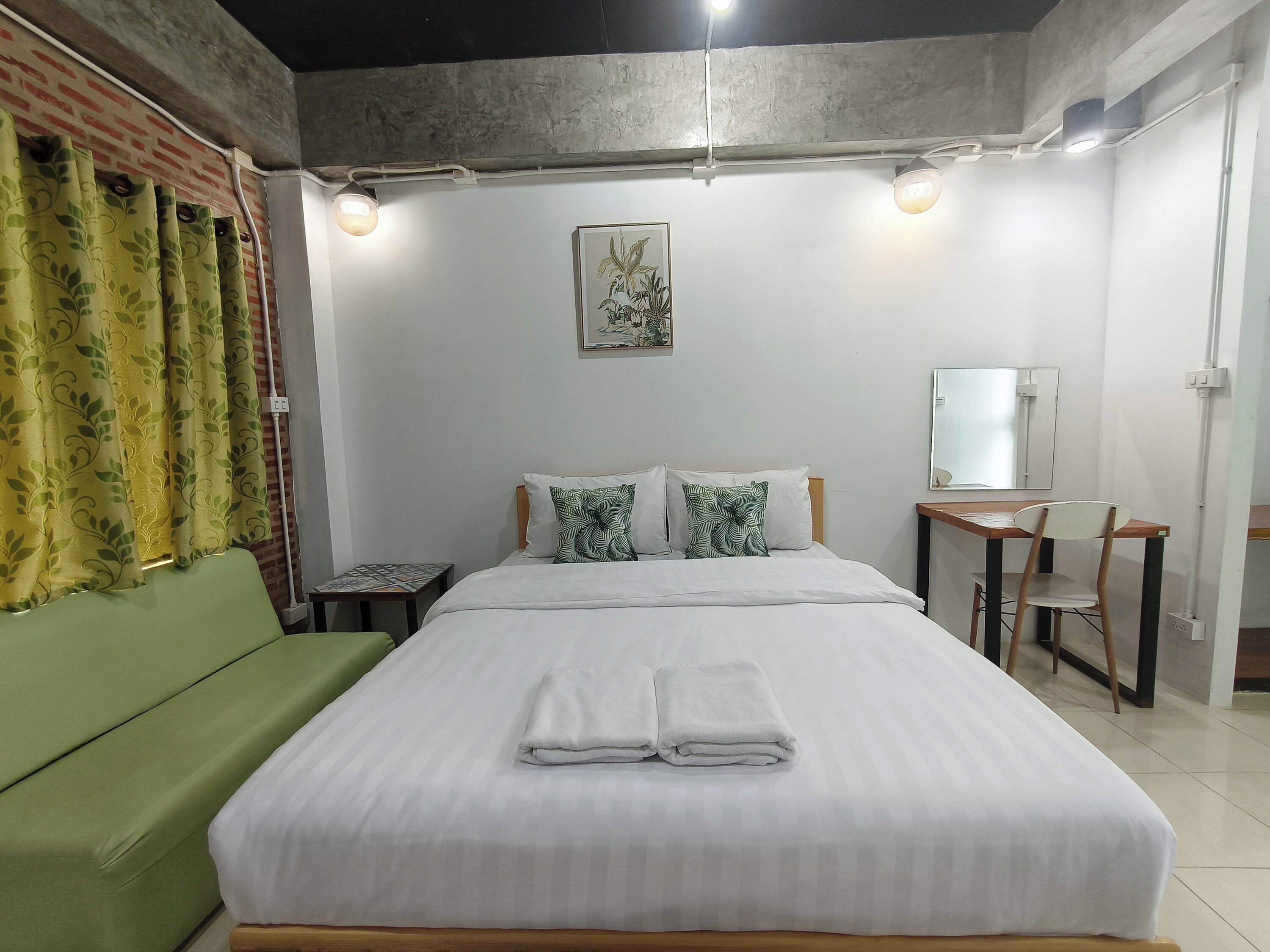 A neatly made bed with white linens, a green sofa, a small table with a mirror, and a wall-mounted picture.