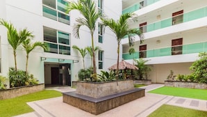 A modern building with a courtyard featuring a central planter, palm trees, and a thatched-roof structure. - Laguna Bay 1  by PSR ASIA (Pattaya)