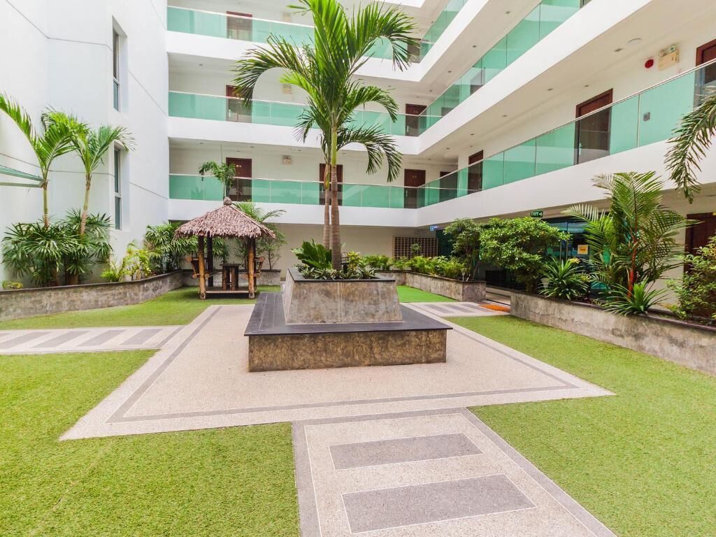 A multi-level atrium with a central garden area, palm trees, and a thatched-roof gazebo.