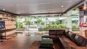 A modern lobby with a leather sofa, a glass wall, and a view of the outdoor garden. - Laguna Bay 1  by PSR ASIA (Pattaya)