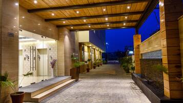 A hotel entrance with a covered walkway, potted plants, and a stone-tiled ground.