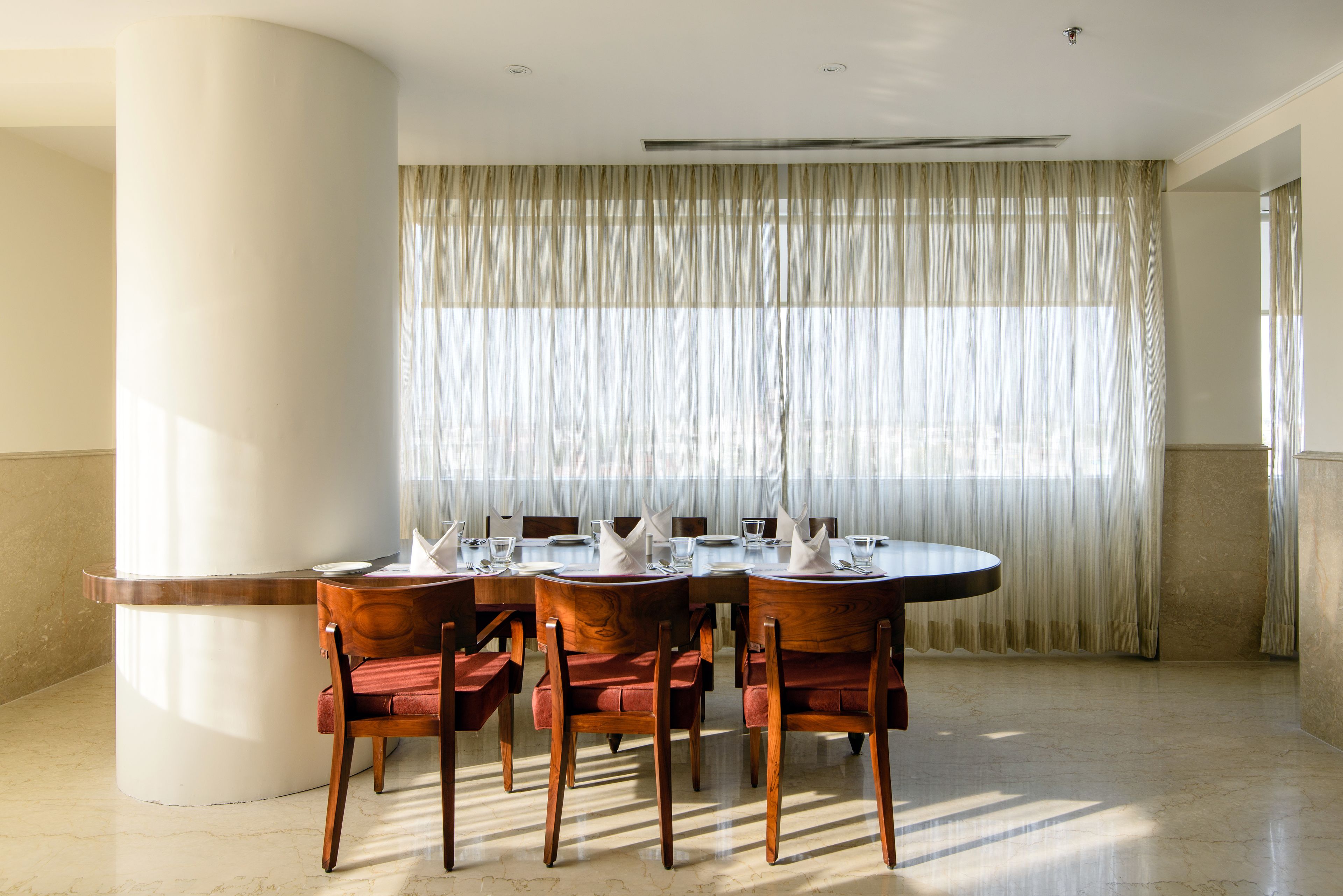 Comedor con una mesa redonda dispuesta para cuatro personas, rodeada de sillas de madera con cojines rojos.