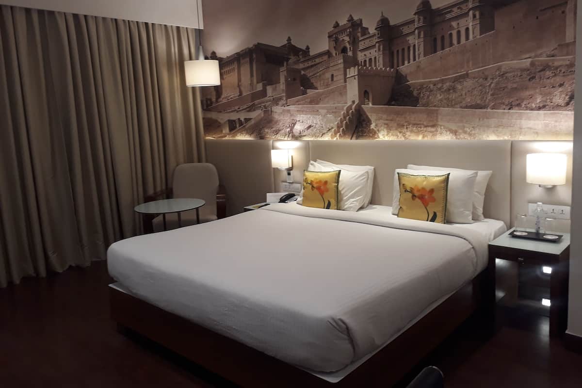 Una habitación de hotel con una cama grande, una silla, una mesita pequeña y un mural en la pared de un edificio histórico.