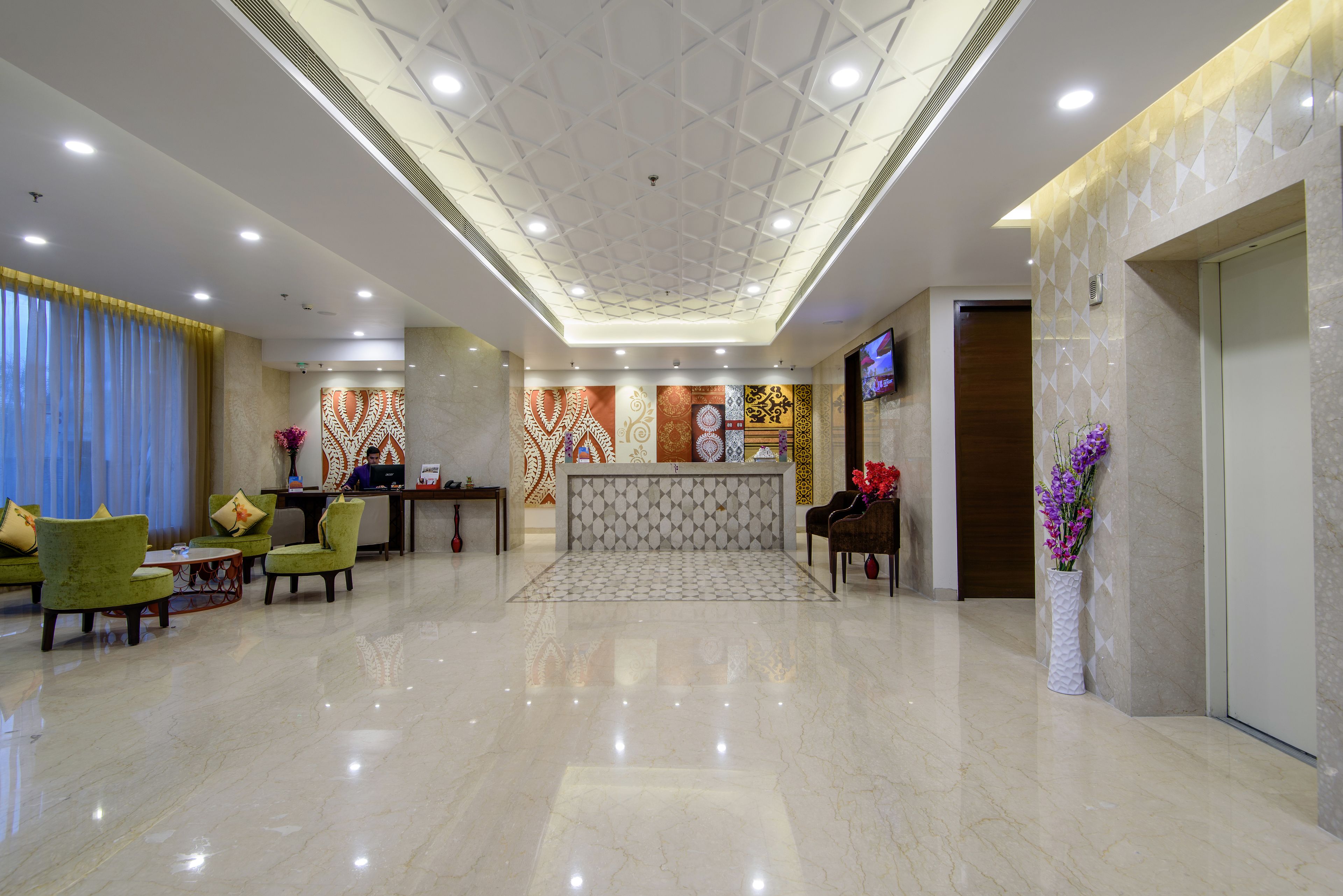 A hotel lobby with a reception desk, green seating area, and a decorative wall.