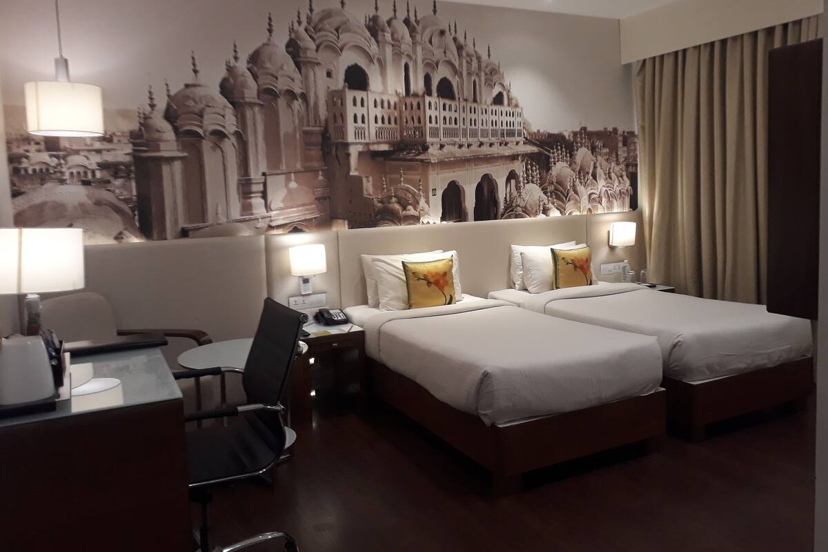 Habitación de hotel con dos camas, un escritorio, una silla y un gran mural en la pared que representa un edificio histórico.