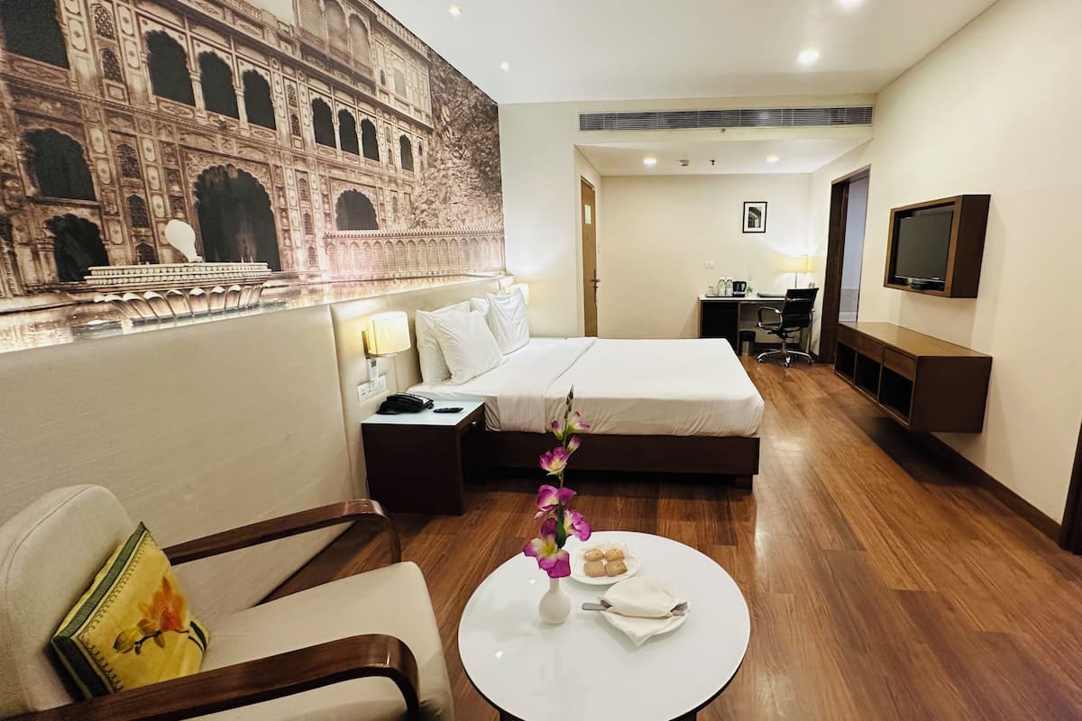 Habitación de hotel con cama, escritorio, silla, televisor y decoración en la pared.