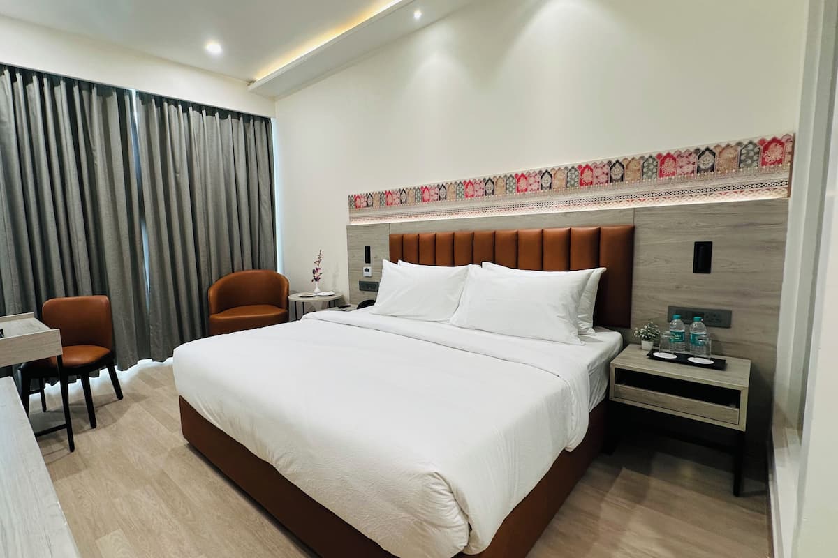 Habitación de hotel con una cama grande, dos sillas, un escritorio y una mesita de noche con lámpara.