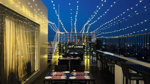 Un salón en la azotea con luces colgantes, un letrero que dice "Sky Lounge" y mesas dispuestas para comer.