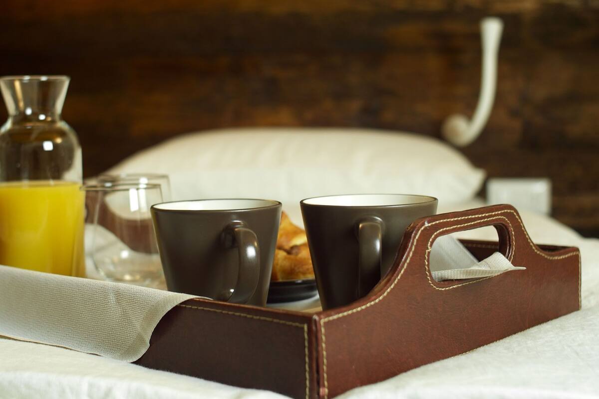 Een ontbijfwagen met een koffiezetapparaat, twee kopjes, een glas sinaasappelsap en een brood.