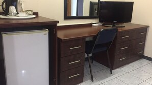 Un pequeño espacio de oficina con escritorio, silla, televisor, refrigerador y cafetera.