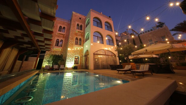 A swimming pool with lounge chairs and umbrellas, surrounded by buildings with arched windows and a stone facade. - Siena Hotel (Ghazir)