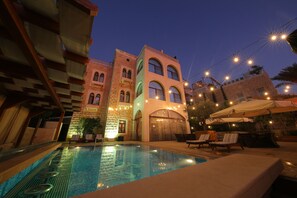 A swimming pool with lounge chairs and umbrellas, surrounded by buildings with arched windows and a stone facade. - Siena Hotel (Ghazir)