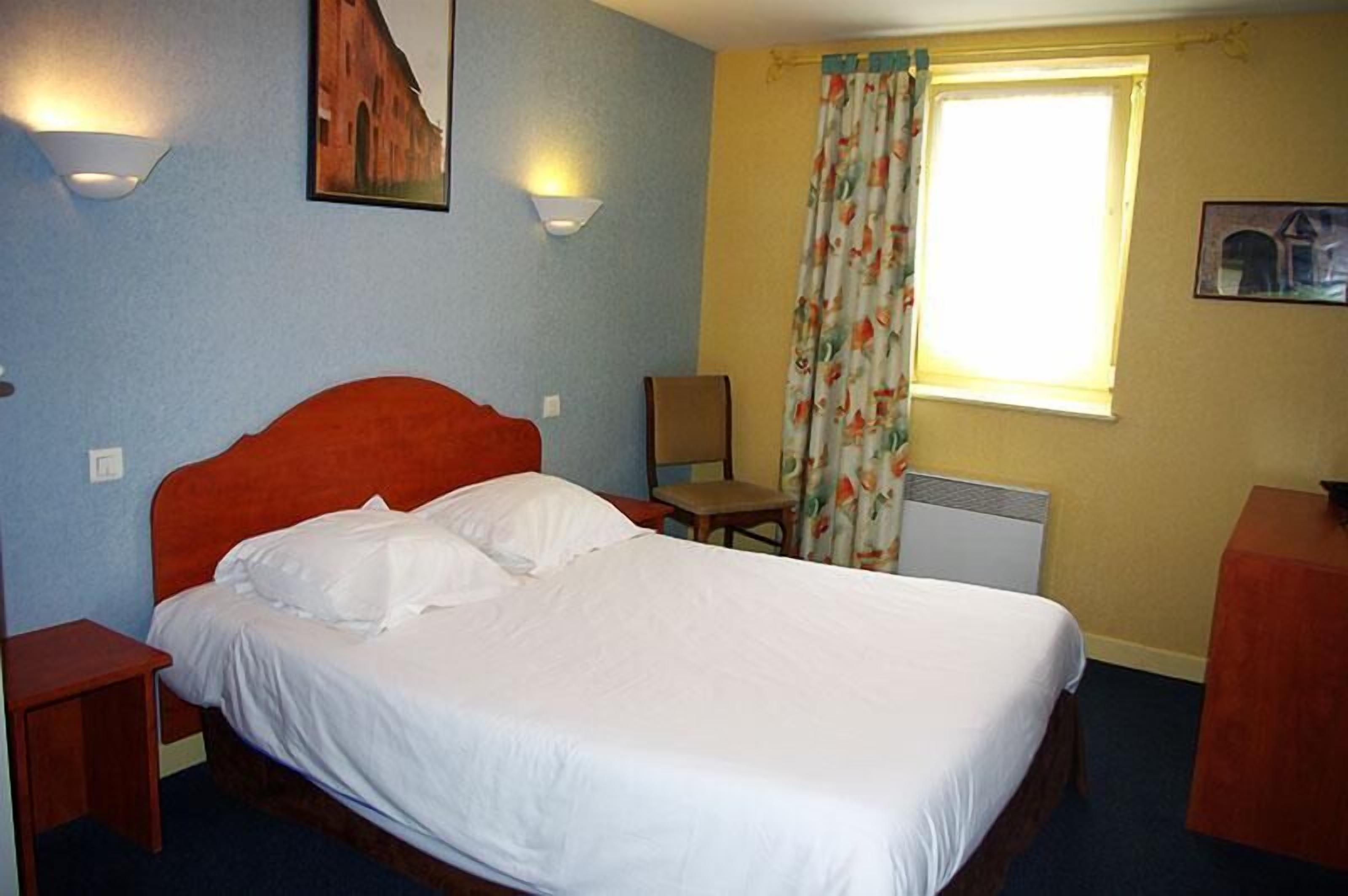 A hotel room with a single bed, a chair, a desk, and a window with curtains.
