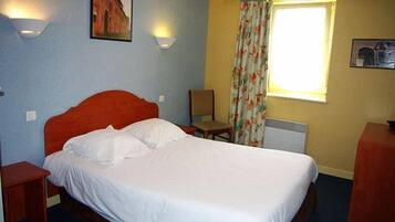 A hotel room with a single bed, a chair, a desk, and a window with curtains.