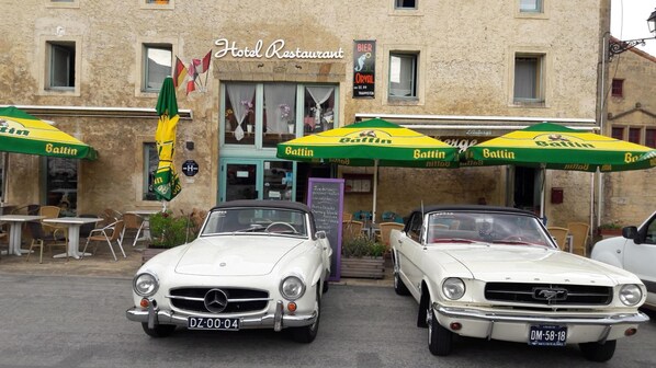 A hotel restaurant with two classic cars parked in front.