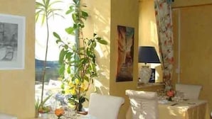 A room with a bed, a chair, a table with a lamp, and a window with a view of palm trees. - Auberge de Marville (Marville)