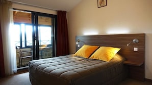 A bedroom with a large bed, a wooden headboard, and a view through a sliding glass door to an outdoor area. - Auberge de Marville (Marville)