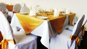 A banquet hall with round tables covered in yellow tablecloths, white chairs with gold sashes, and white table settings. - Mahaweli Regent Hotel (Kandy)
