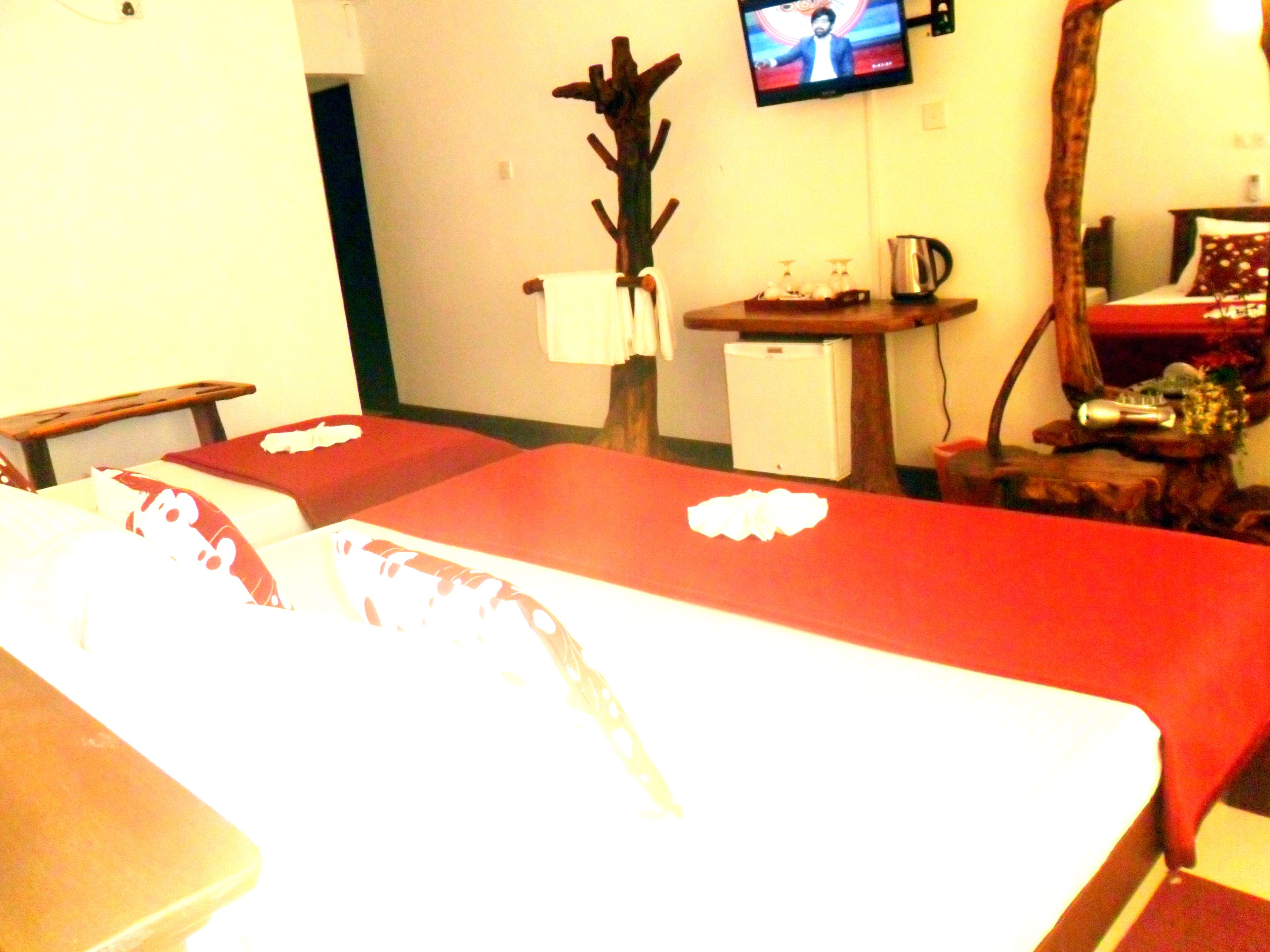 A hotel room with two beds, a television on the wall, a small refrigerator, and a wooden chair.