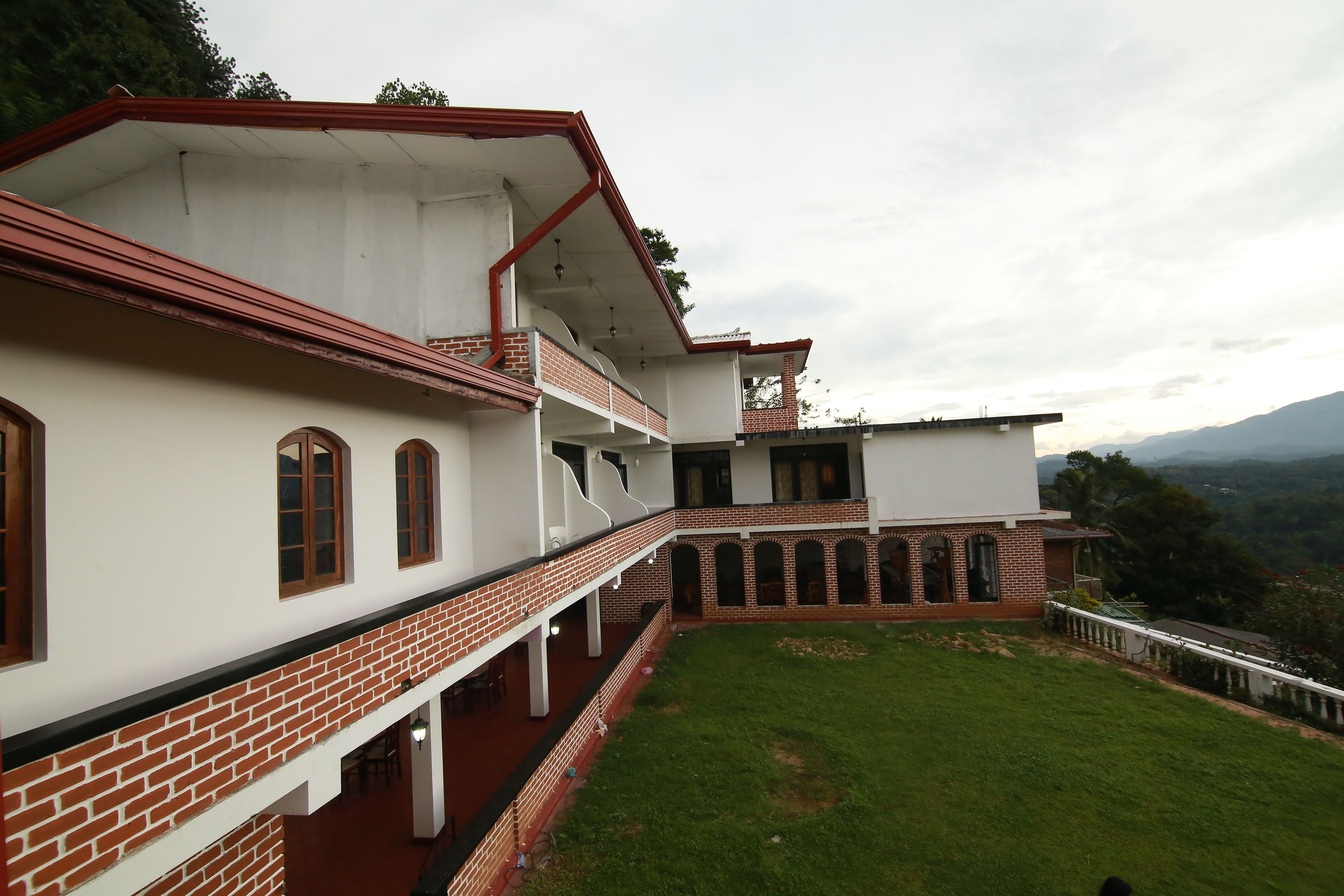 A multi-story building with a flat roof, a brick lower section, and a white upper section. It features multiple windows and a covered outdoor area with a grassy courtyard.