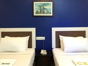 Habitación de hotel con dos camas, una mesita de noche con teléfono y un cuadro de un paisaje urbano en la pared.