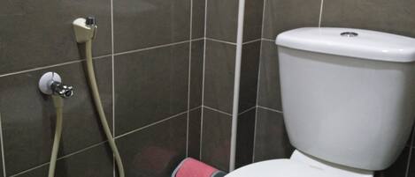 A bathroom with a toilet, a shower hose, and a trash bin.