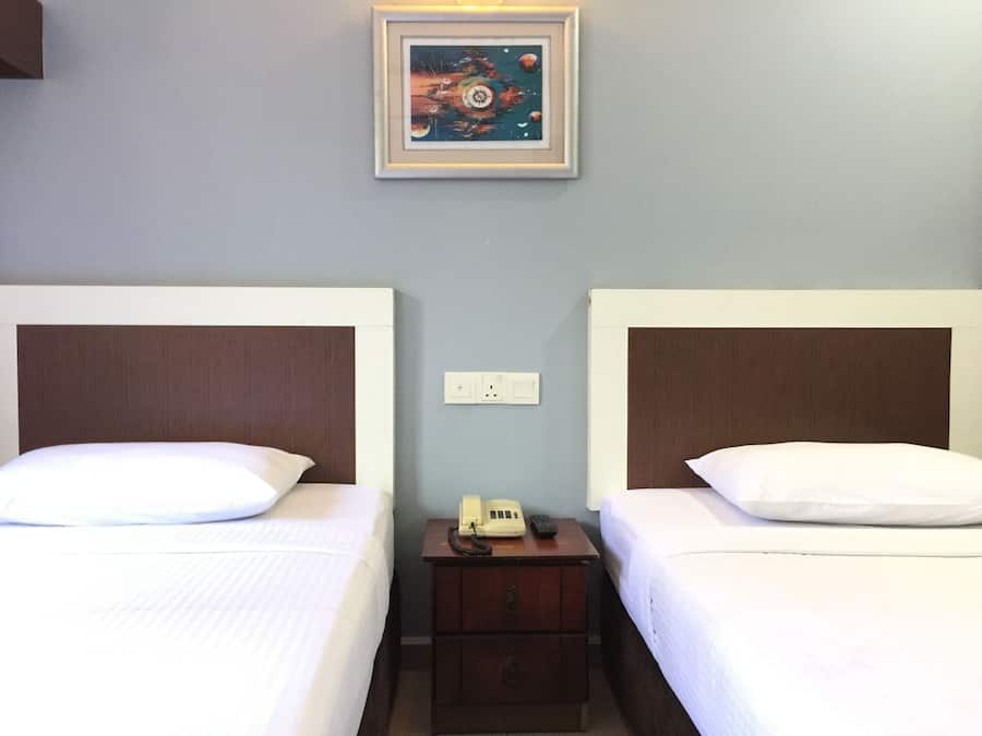 Une chambre d’hôtel avec deux lits, une table de chevet avec un téléphone et un tableau encadré au mur.
