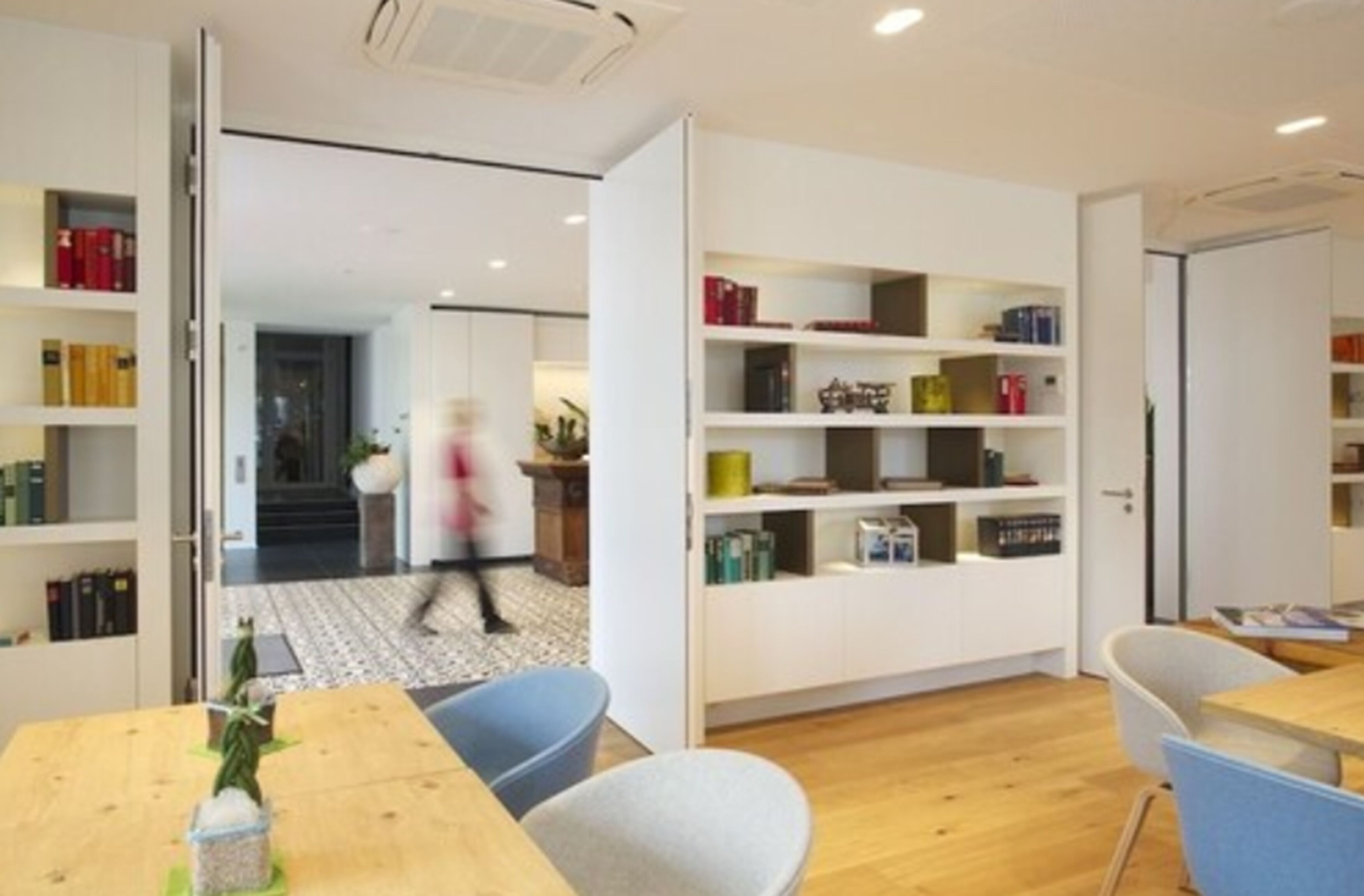 A modern library with open shelving, a wooden table, and chairs.