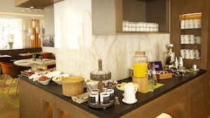 Un buffet de petit-déjeuner proposant une variété d’aliments et de boissons, un coin café, ainsi qu’un espace détente avec des chaises et une table.