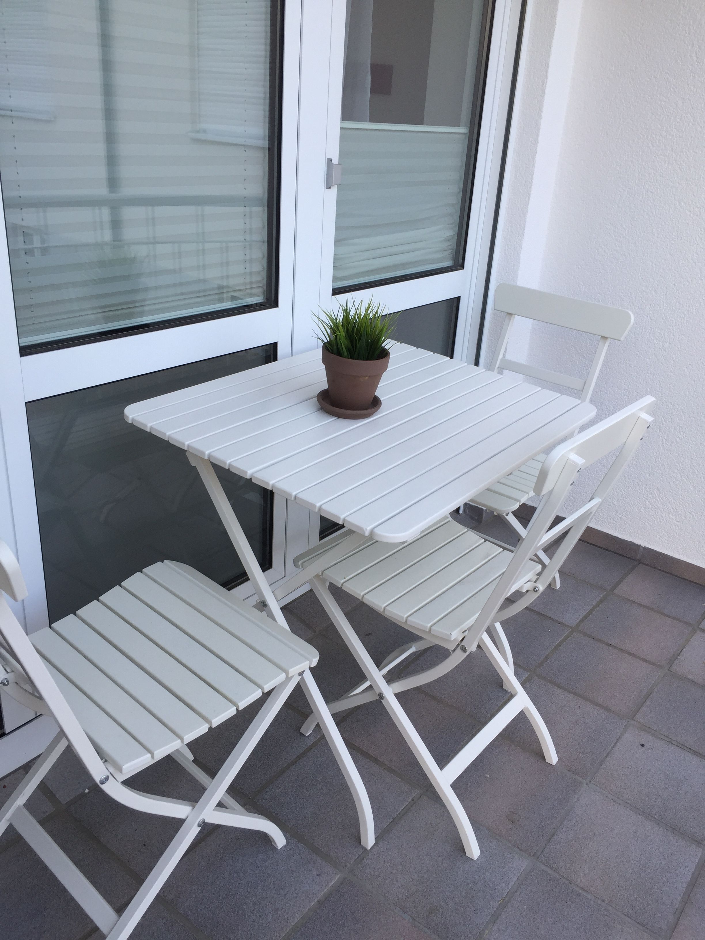 Mesa y sillas de metal blanco en un balcón con una planta en maceta.