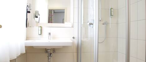A bathroom with a glass-enclosed shower, a sink with a mirror, and patterned floor tiles.