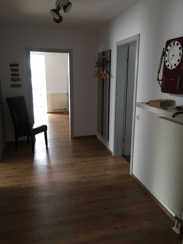 A spacious room with wooden flooring, a chair, a radiator, a clock, and a door leading to another room. - Illertisser Hof (Illertissen)