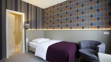 A hotel room with a bed, a chair, a shower, and a patterned wall.