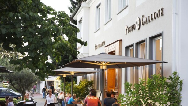 Un espace extérieur aménagé pour les repas, avec des tables et des parasols, situé devant un bâtiment sur lequel est apposée une enseigne indiquant « Piero & Callone ».