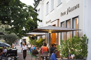 An outdoor dining area with tables and umbrellas in front of a building with a sign that reads "Piero & Callone". - Illertisser Hof (Illertissen)