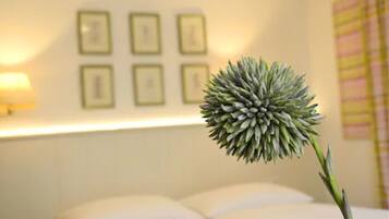A room with a bed, a wall with framed pictures, and a potted plant.