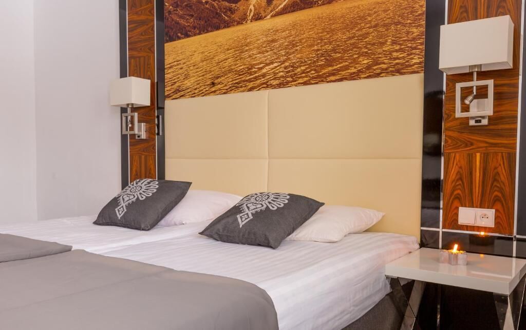 Une chambre d’hôtel avec un lit, deux oreillers, une table de chevet avec une lampe et un luminaire fixé au mur.