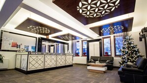 A modern living room with a central island, dark wooden flooring, and a ceiling with geometric light fixtures.
