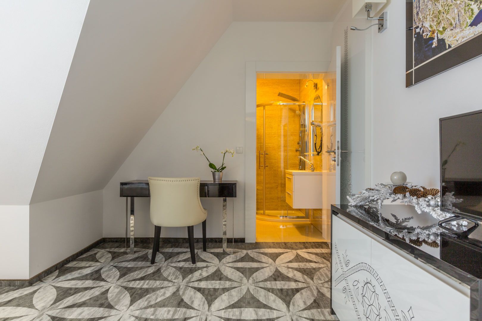 A modern bathroom with a glass shower enclosure, a white chair, and a decorative mirror.