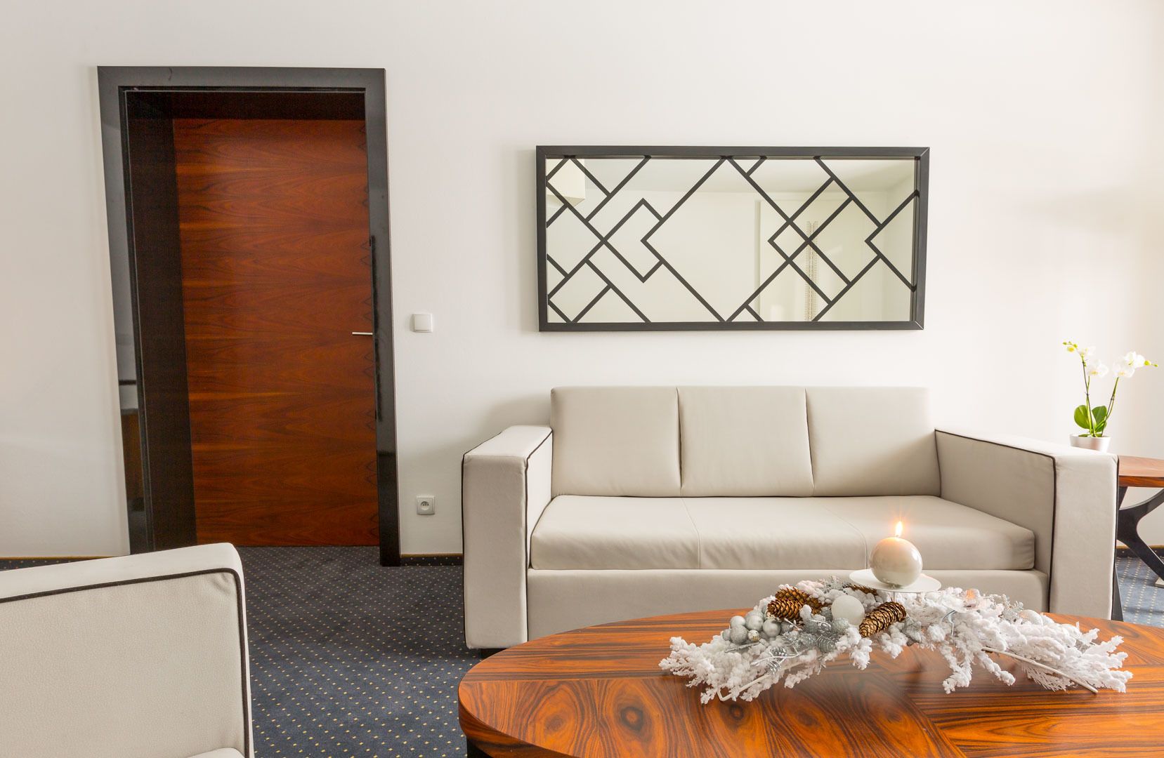 A modern living room with a beige sofa, a wooden coffee table with a decorative centerpiece, and a geometric mirror on the wall.