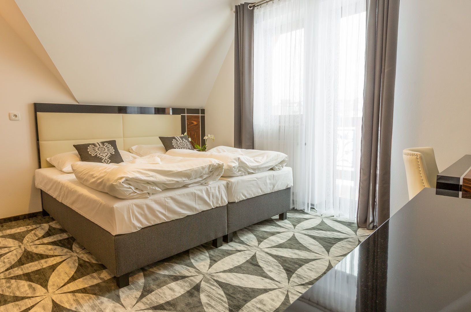 Een netjes opgemaakt bed met witte lakens en decoratieve kussens, een modern hoofdbord en een vloer met een patroon.