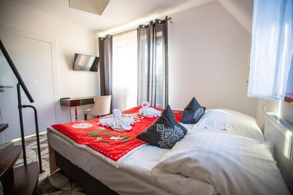 Ein Hotelzimmer mit Bett, Schreibtisch, Stuhl, Fernseher und einem Fenster mit Vorhängen.