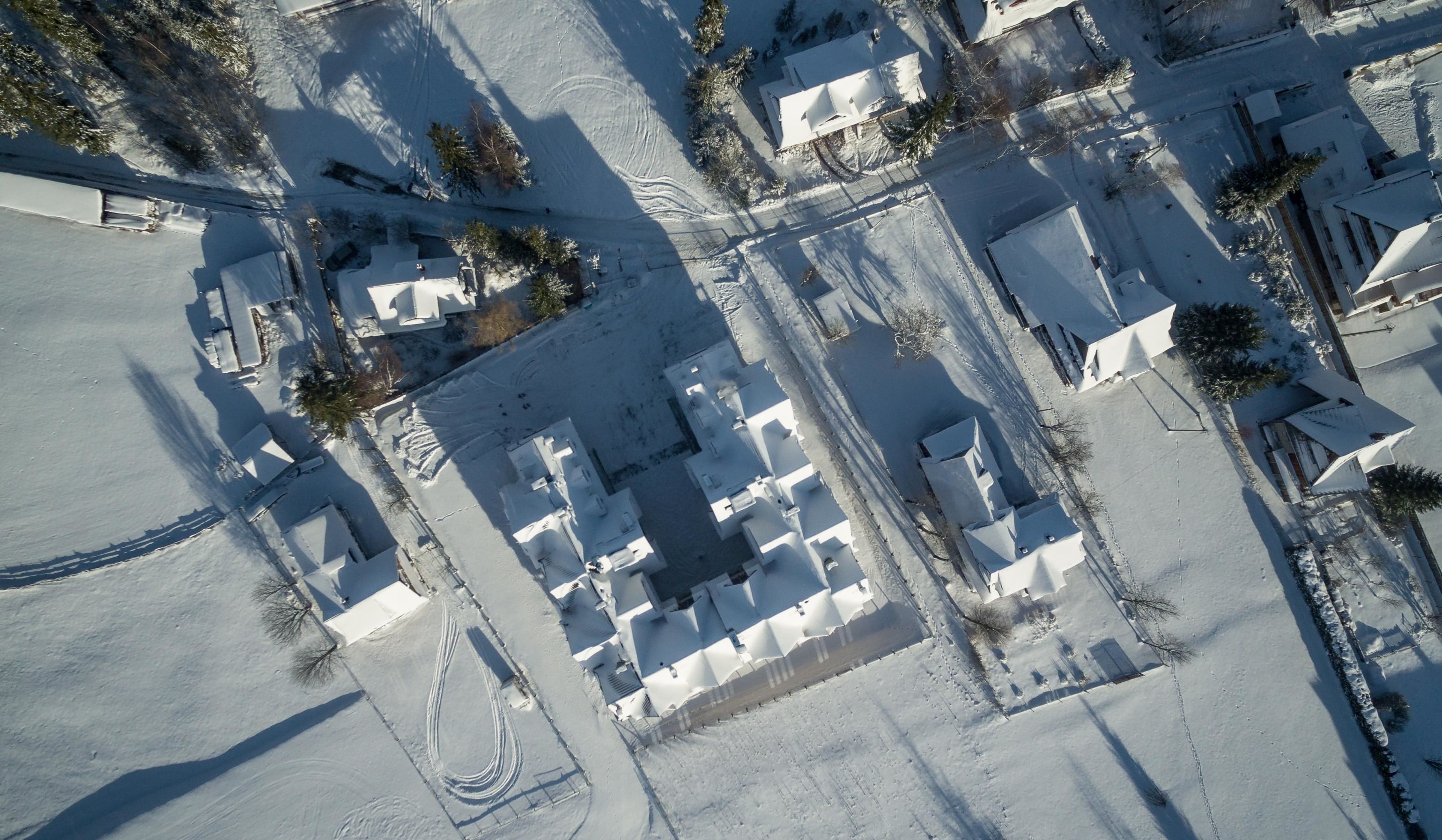 Vue aérienne d’un quartier résidentiel enneigé, avec des maisons, des rues et quelques arbres.