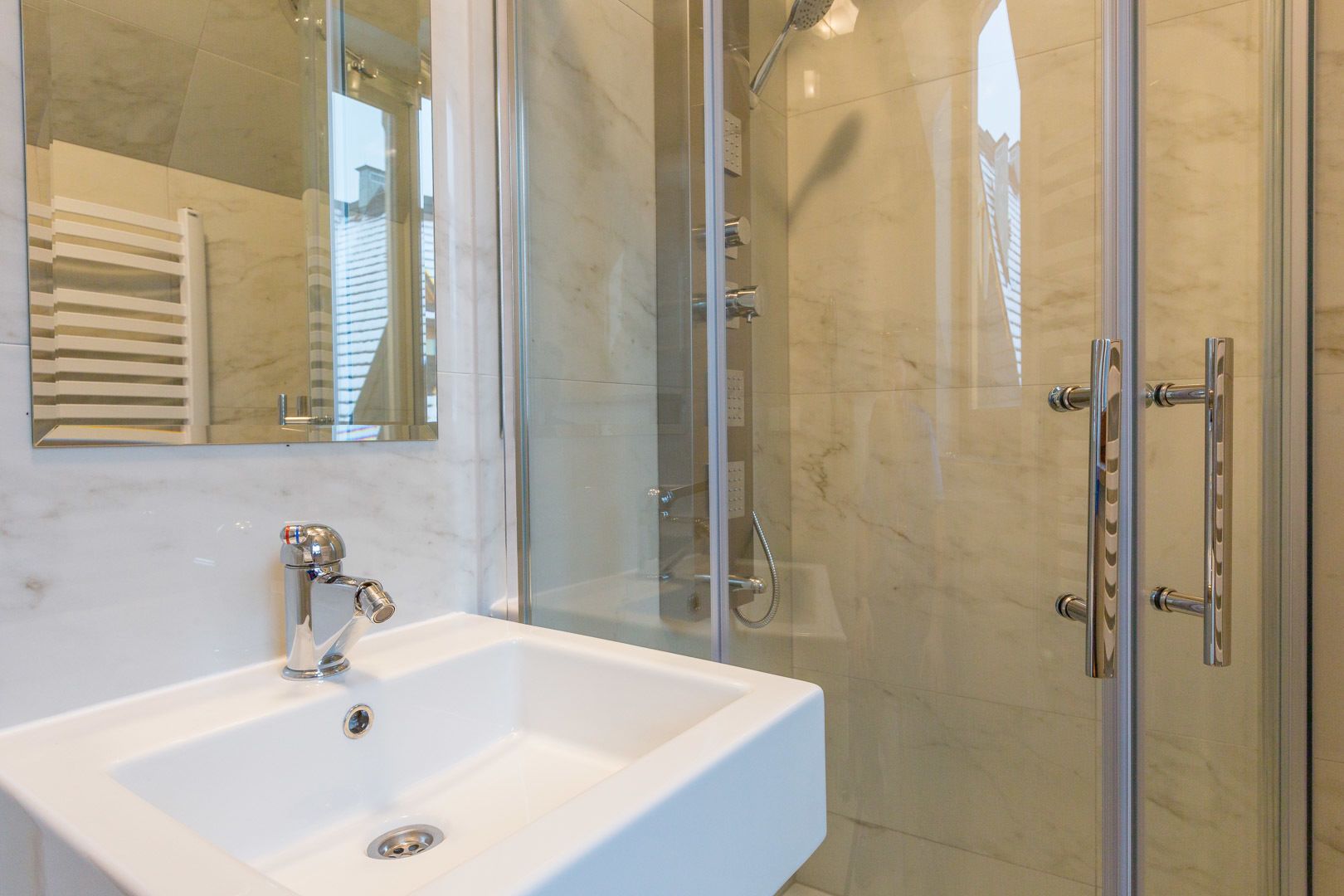 Ein modernes Badezimmer mit einem weißen Waschbecken, einer Duschkabine aus Glas und einem großen Spiegel.