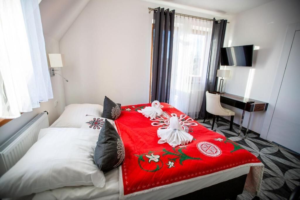 A hotel room with a bed, a desk, a chair, a TV, and a window with curtains.