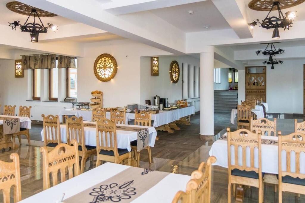 A spacious dining area with wooden tables and chairs, decorative wall art, and chandeliers.