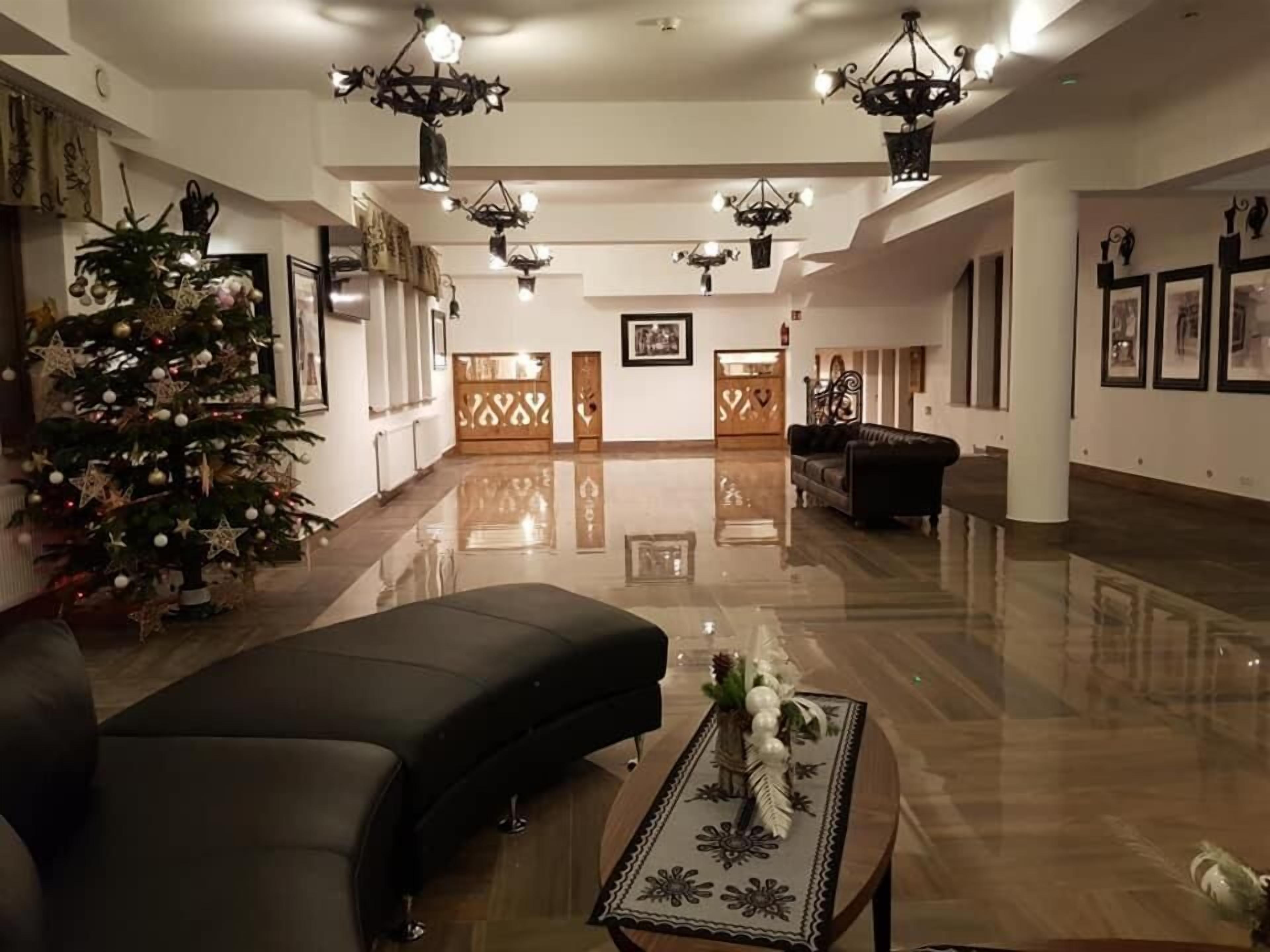 Un vestíbulo amplio con suelo pulido, un árbol de Navidad, un sofá negro y una mesa de centro con adornos.
