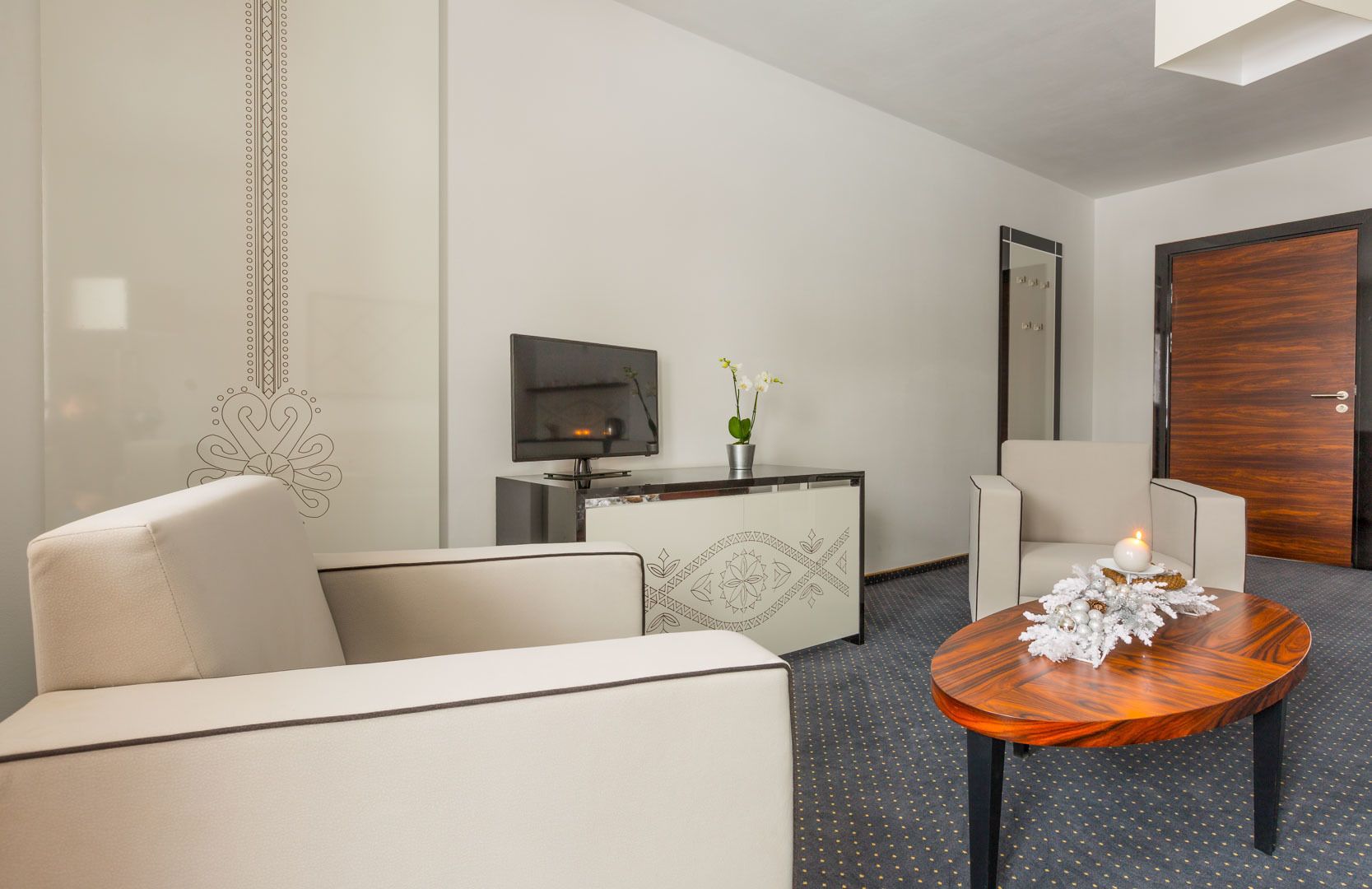Une chambre d’hôtel moderne avec un canapé, une petite table sur laquelle est posée une bougie, une télévision et une plante décorative.